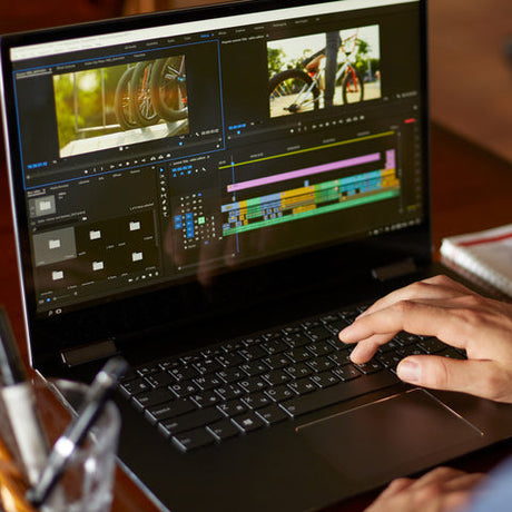 A man sitting at a desk with a laptop. The laptop screen displays a video editing program and two images of a bike.