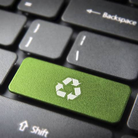 Close-up of a black laptop keyboard with a green key with the recycling symbol. The keys "backspace" and "shift" are blurry.